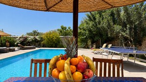 Escena junto a la piscina con una mesa, sillas y un frutero.