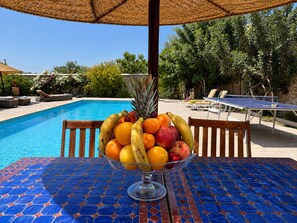 Ein Poolbereich mit Tisch, Stühlen und einer Obstschale.