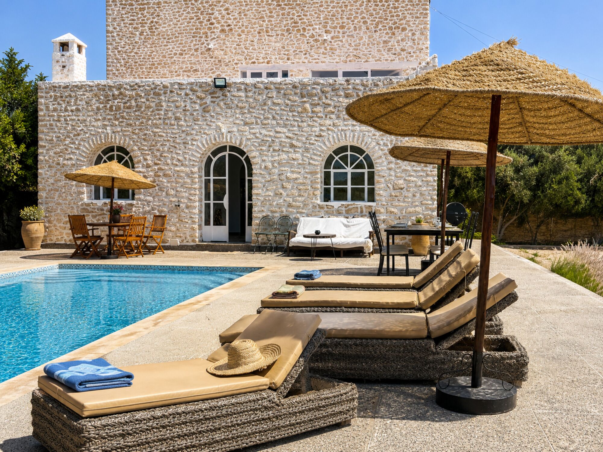 Un bâtiment en pierre doté d’une piscine, de chaises longues et de parasols.