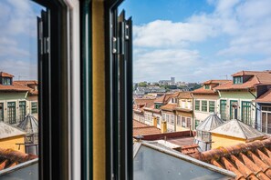 Blick auf Gebäude mit terrakottafarbenen Dächern und grünen Fensterrahmen, einem klaren Himmel und einer entfernten Skyline.