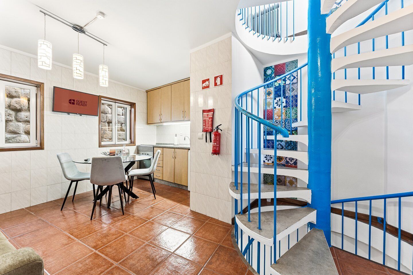 Una cocina moderna con zona de comedor, una escalera en espiral con barandillas azules y un extintor en la pared.