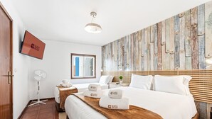 Quarto de hotel com uma cama, mesa de cabeceira, televisão de tela plana, obra de arte na parede e uma janela.