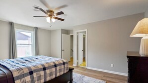 A bedroom with a bed, a ceiling fan, a window with curtains, and a door leading to another room. - Hoover Furnished Stay | Families & Pros (Birmingham)