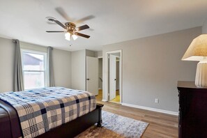 A bedroom with a bed, a ceiling fan, a window with curtains, and a door leading to another room. - Hoover Furnished Stay | Families & Pros (Birmingham)