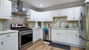 A modern kitchen with white cabinets, stainless steel appliances, and a patterned backsplash. - Hoover Furnished Stay | Families & Pros (Birmingham)