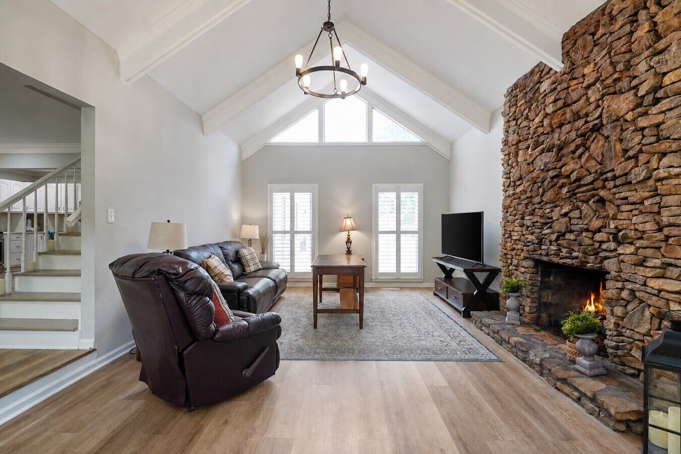 A spacious living room with a stone fireplace, a leather sofa, and a chandelier.