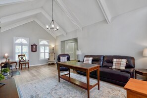 A spacious living room with a high ceiling, a dark leather sofa, a wooden coffee table, and a chandelier. - Hoover Furnished Stay | Families & Pros (Birmingham)