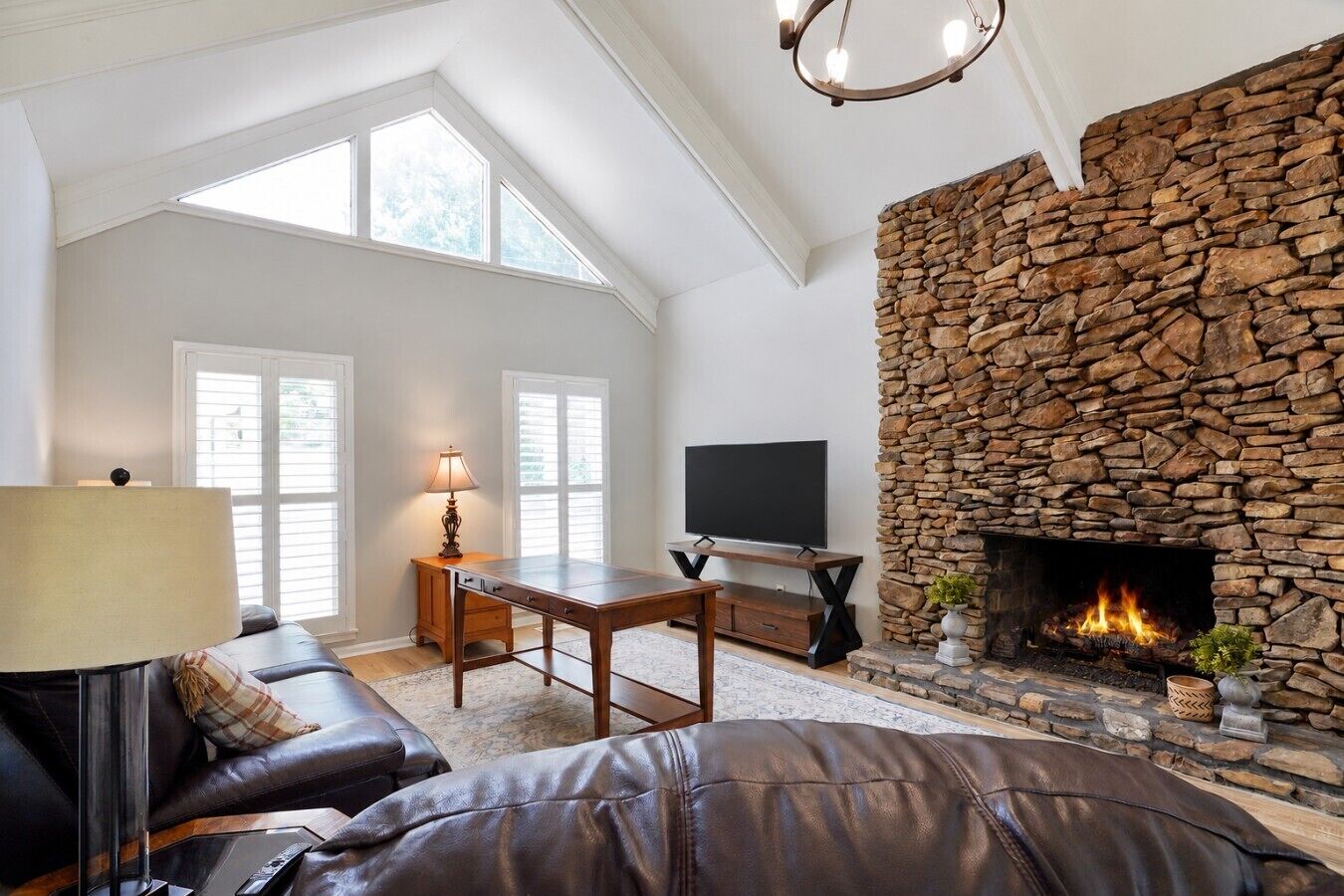 Una sala de estar con chimenea de piedra, un televisor de pantalla plana, un sofá de cuero y una mesa con lámpara.