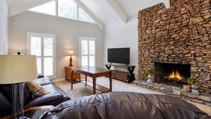 A living room with a stone fireplace, a flat-screen TV, a leather sofa, and a table with a lamp. - Hoover Furnished Stay | Families & Pros (Birmingham)