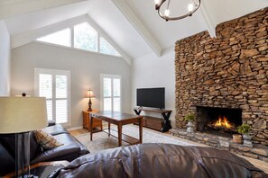 A living room with a stone fireplace, a flat-screen TV, a leather sofa, and a table with a lamp. - Hoover Furnished Stay | Families & Pros (Birmingham)