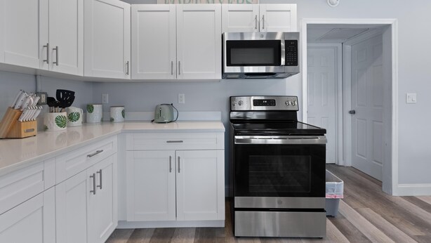 A modern kitchen with white cabinets, a stainless steel oven, a microwave, and a toaster. - Dune Your Thing A&B (Fort Myers Beach)