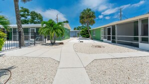 A courtyard with a pathway, palm trees, and a building with large windows. - Dune Your Thing A&B (Fort Myers Beach)