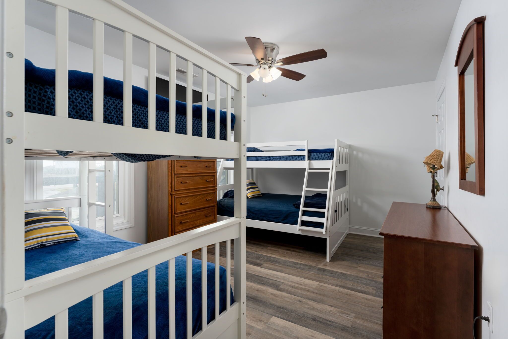 A bedroom with bunk beds, a wooden dresser, a ceiling fan, and a mirror.