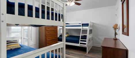 A bedroom with bunk beds, a wooden dresser, a ceiling fan, and a mirror.