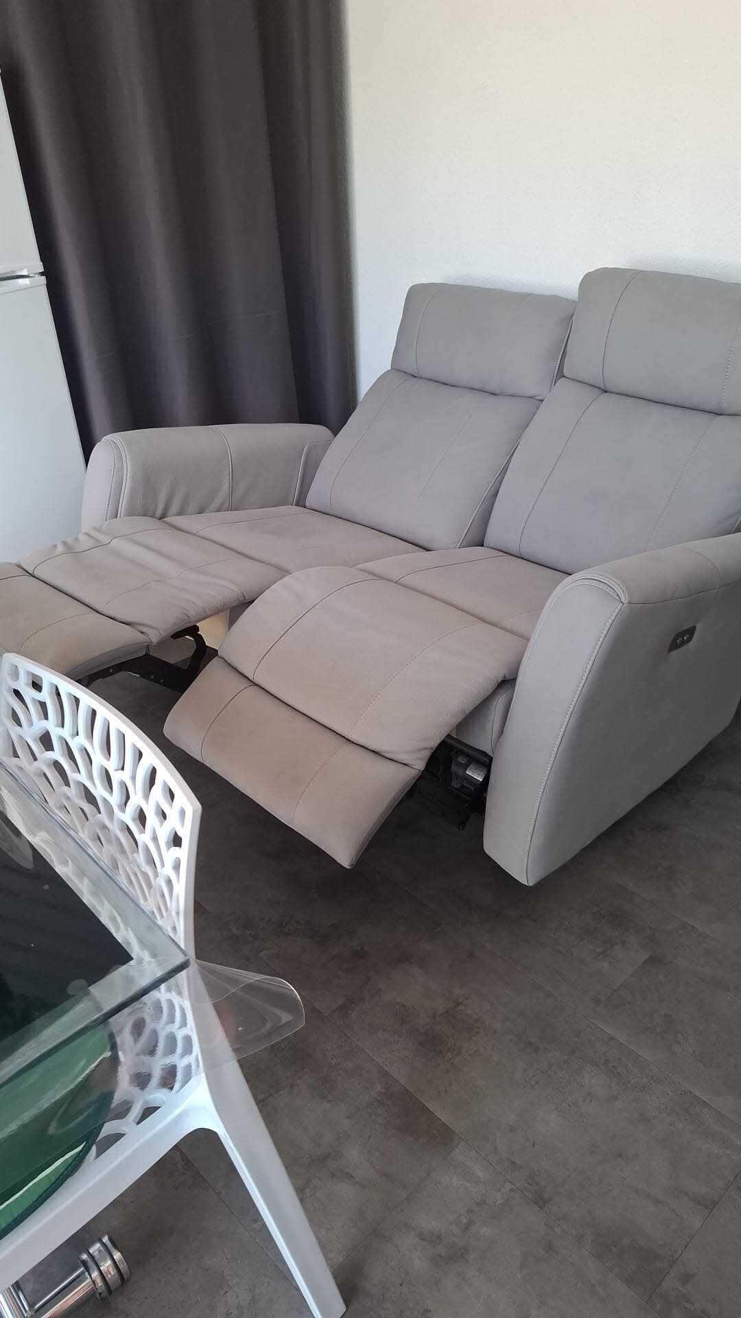 A reclining sofa with a white frame and a glass table in front.