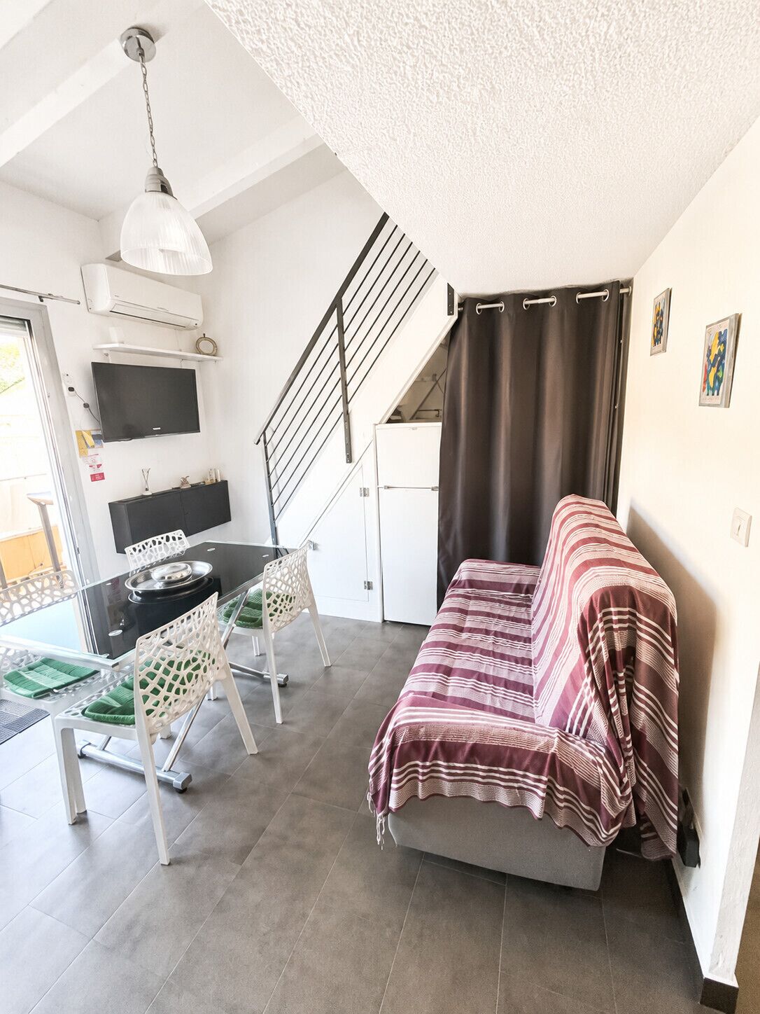 A compact living space with a sofa, dining table, chairs, a TV, and a staircase.