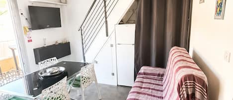 Un espace de vie compact comprenant un canapé, une table à manger, des chaises, un téléviseur et un escalier.