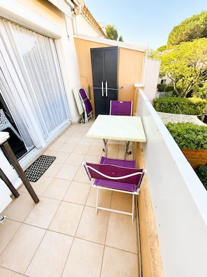 A small outdoor balcony with a table and two chairs, a sliding door, and a black refrigerator. - EUREKA 238  - Appartement -Piscine Terrasse - Plages à pied (Agde)