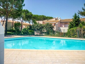 A swimming pool with a tiled deck, surrounded by greenery and buildings with terracotta roofs. - EUREKA 238  - Appartement -Piscine Terrasse - Plages à pied (Agde)