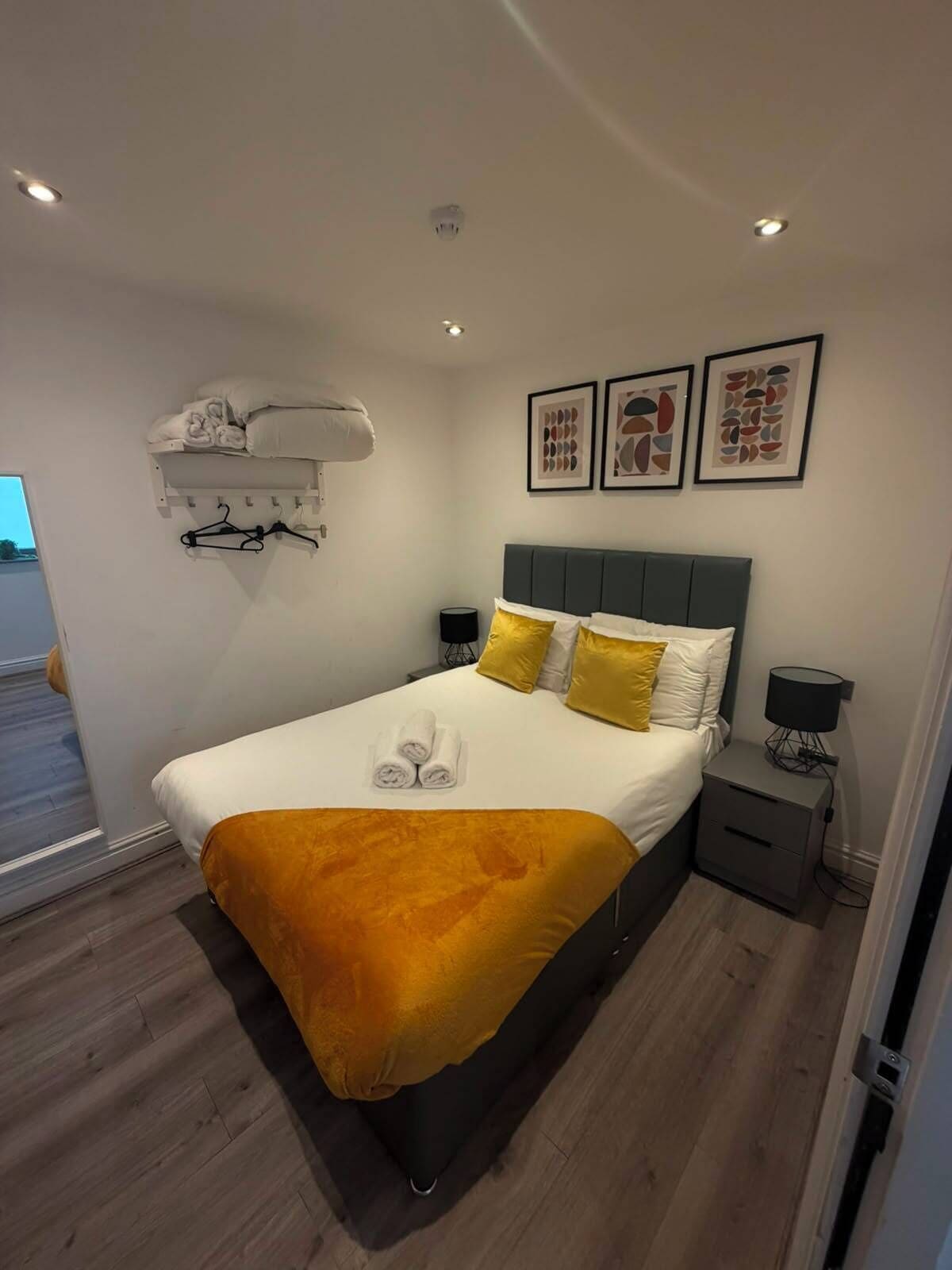 A modern hotel room with a bed, bedside tables, a wall-mounted air conditioner, and artwork.