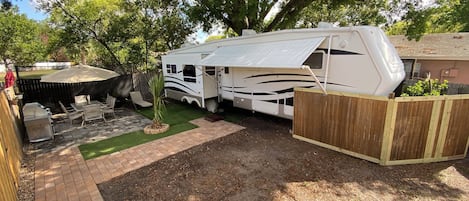A recreational vehicle (RV) parked in a backyard with a patio area, outdoor furniture, and a wooden fence.