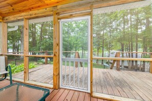A wooden deck with a glass door leading to a forested area. - Waters Edge| Boat Lift+Fenced Yard+Kayaks+PingPong (Littleton)
