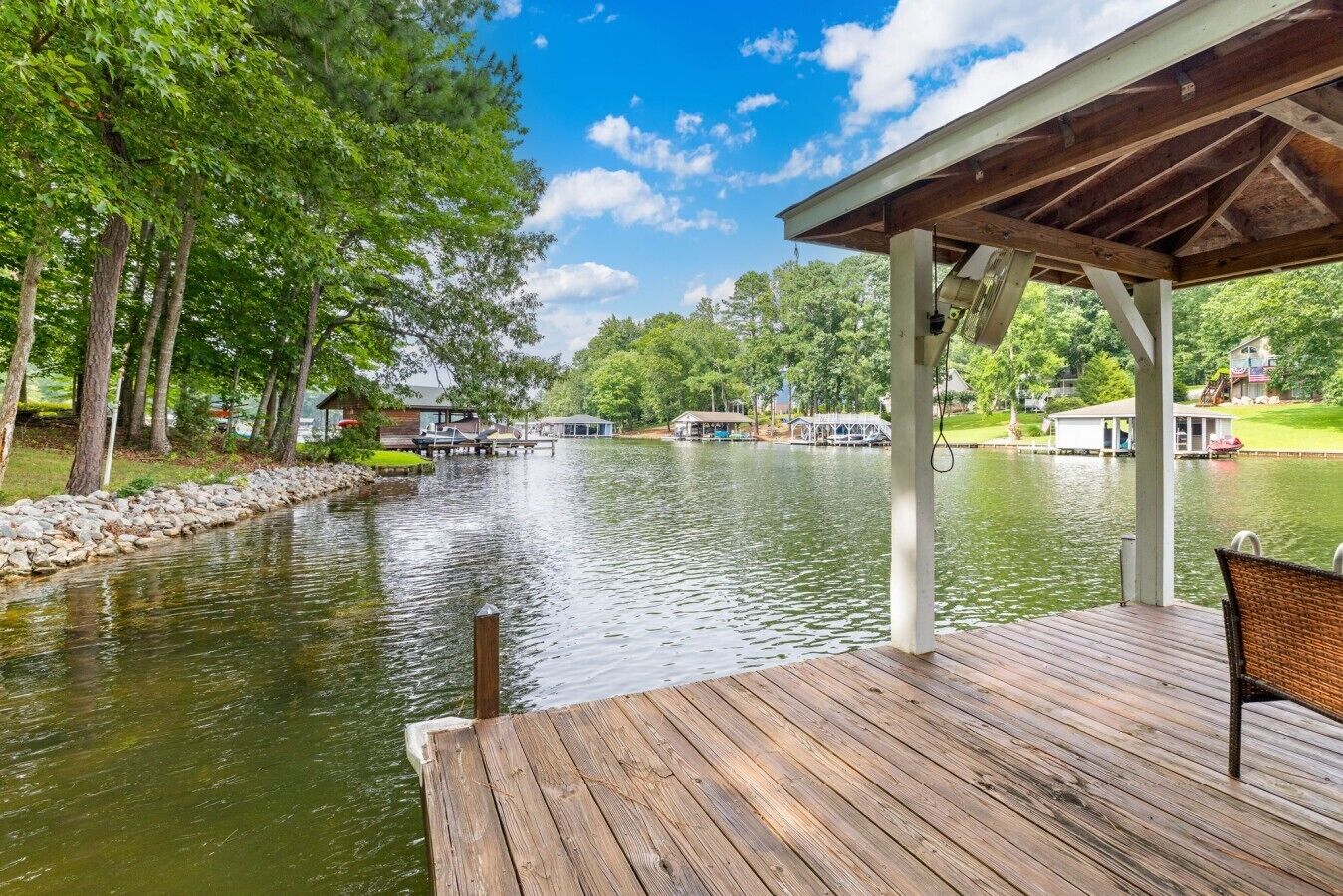 A wooden deck with a view of a river, docked boats, and a gazebo.
