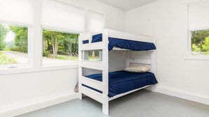 Una cama litera en una habitación con paredes blancas y ventanas grandes.