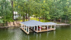 Una casa flotante amarrada con un porche cubierto y zona de estar, rodeada de árboles y agua.