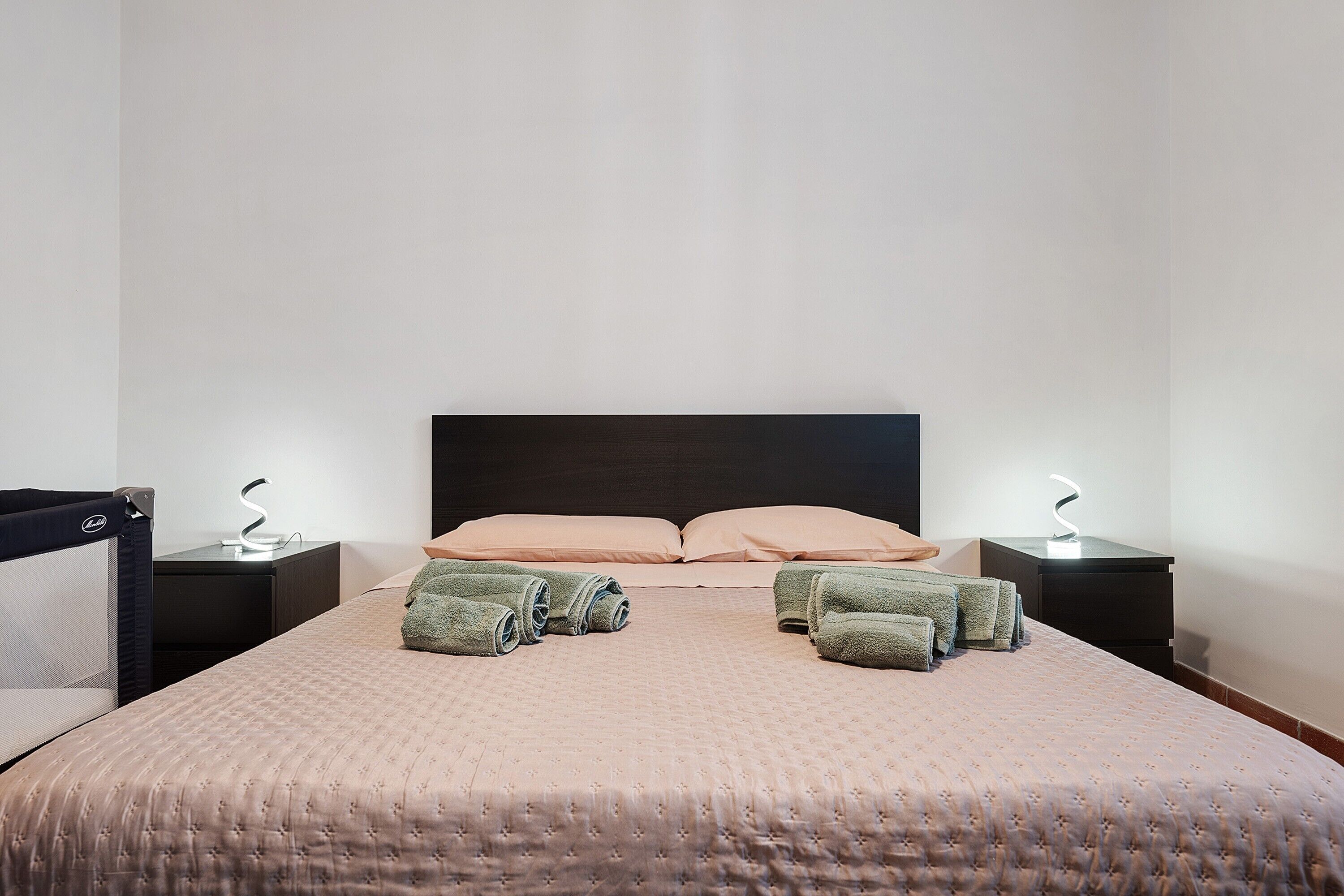 A neatly made bed with a headboard, two bedside tables with lamps, and a chair.