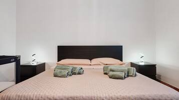 A neatly made bed with a headboard, two bedside tables with lamps, and a chair.