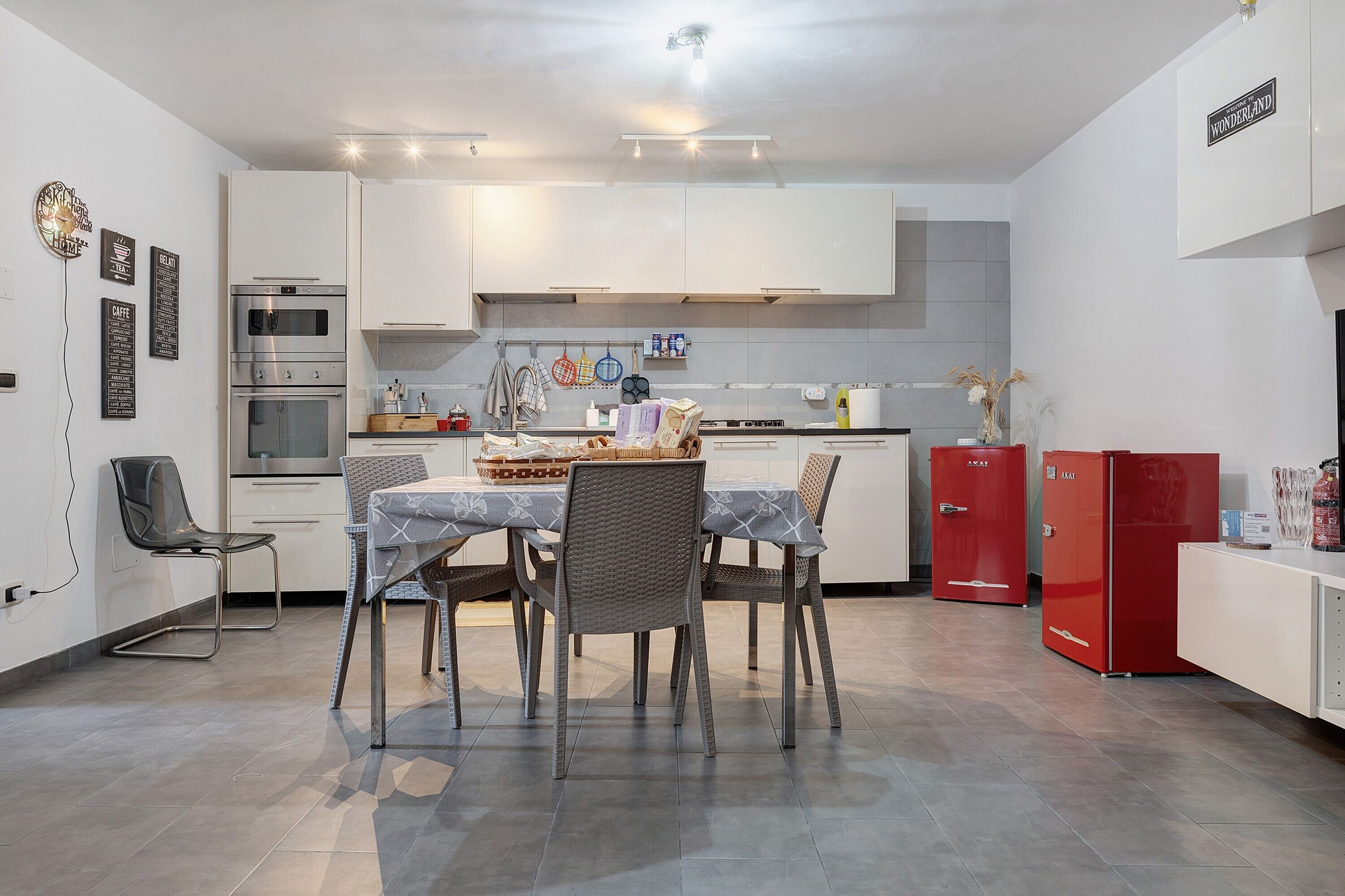 Uma cozinha moderna com armários brancos, uma mesa de jantar com cadeiras e uma geladeira vermelha.