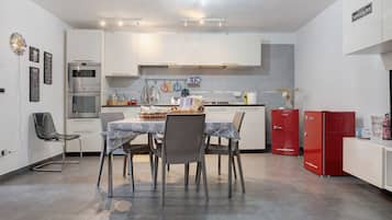 Uma cozinha moderna com armários brancos, uma mesa de jantar com cadeiras e uma geladeira vermelha.