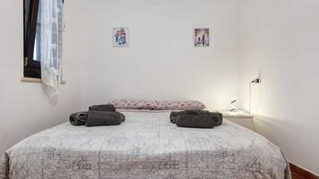Un dormitorio con una cama, dos almohadas, una ventana con cortina y dos cuadros en la pared.