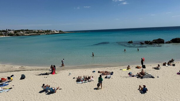 A beach with clear turquoise water, people sunbathing, and a distant shoreline with buildings. - Holiday Home 'Dal Cappellaio Matto' with Private Terrace, Wi-Fi and Air Conditioning (Taranto)