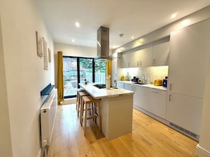 Una cucina moderna con isola centrale, sgabelli in legno e vista sul giardino attraverso ampie finestre.