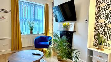 Ein Wohnzimmer mit blauem Sessel, rundem Couchtisch, Kamin und Wand-Fernseher.