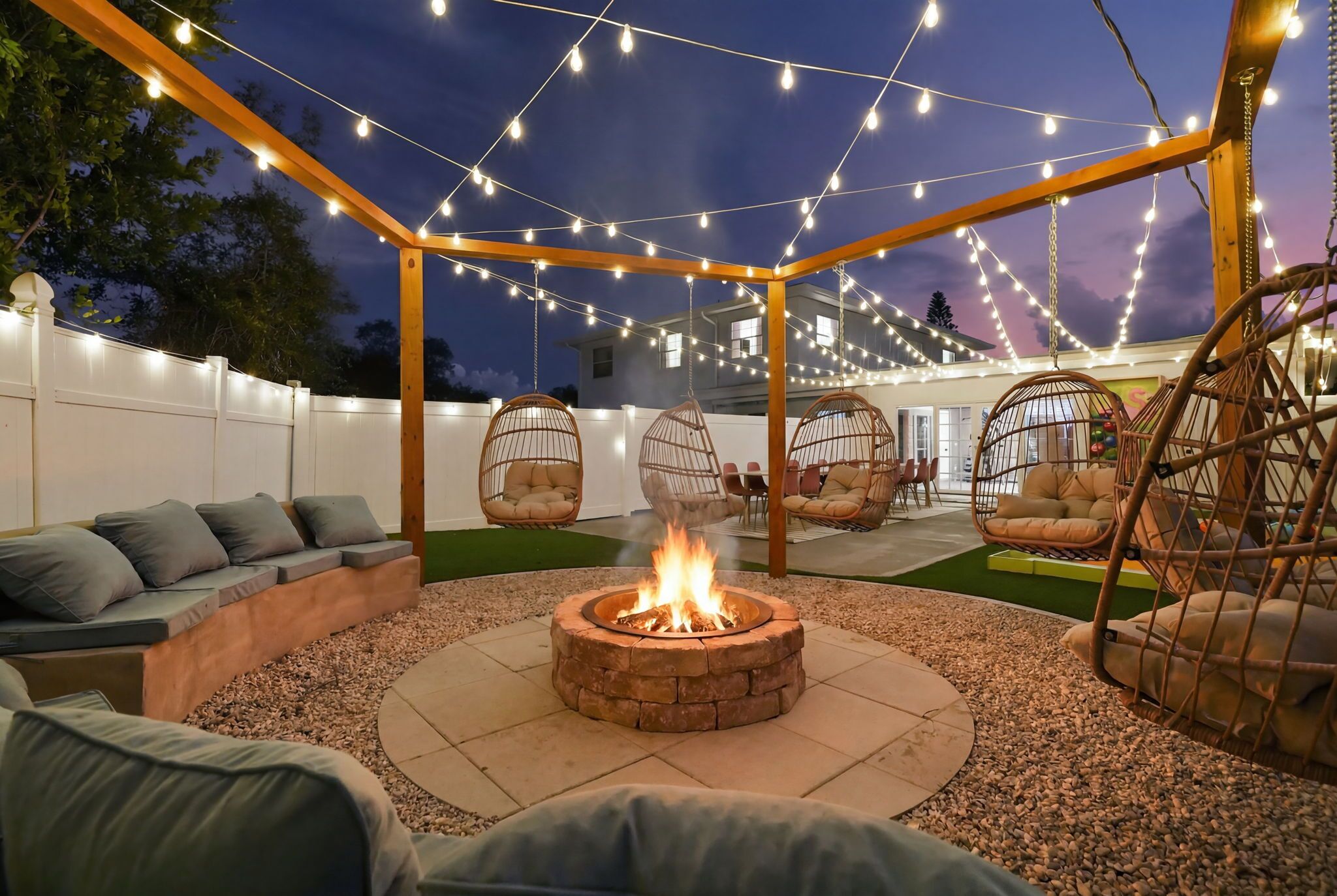 Un patio al aire libre con una fogata, asientos e iluminación colgante.