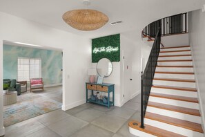 A modern interior with a staircase, a round mirror, a teal console table, and a green wall with a 'High Tide Retreat' sign. - Sauna, Pickleball, Heated Pool, gym, Hot Tub and Games Retreat! (Largo)