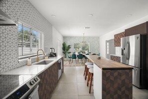 A modern kitchen with a central island, a built-in refrigerator, and a dining area with chairs. - Sauna, Pickleball, Heated Pool, gym, Hot Tub and Games Retreat! (Largo)