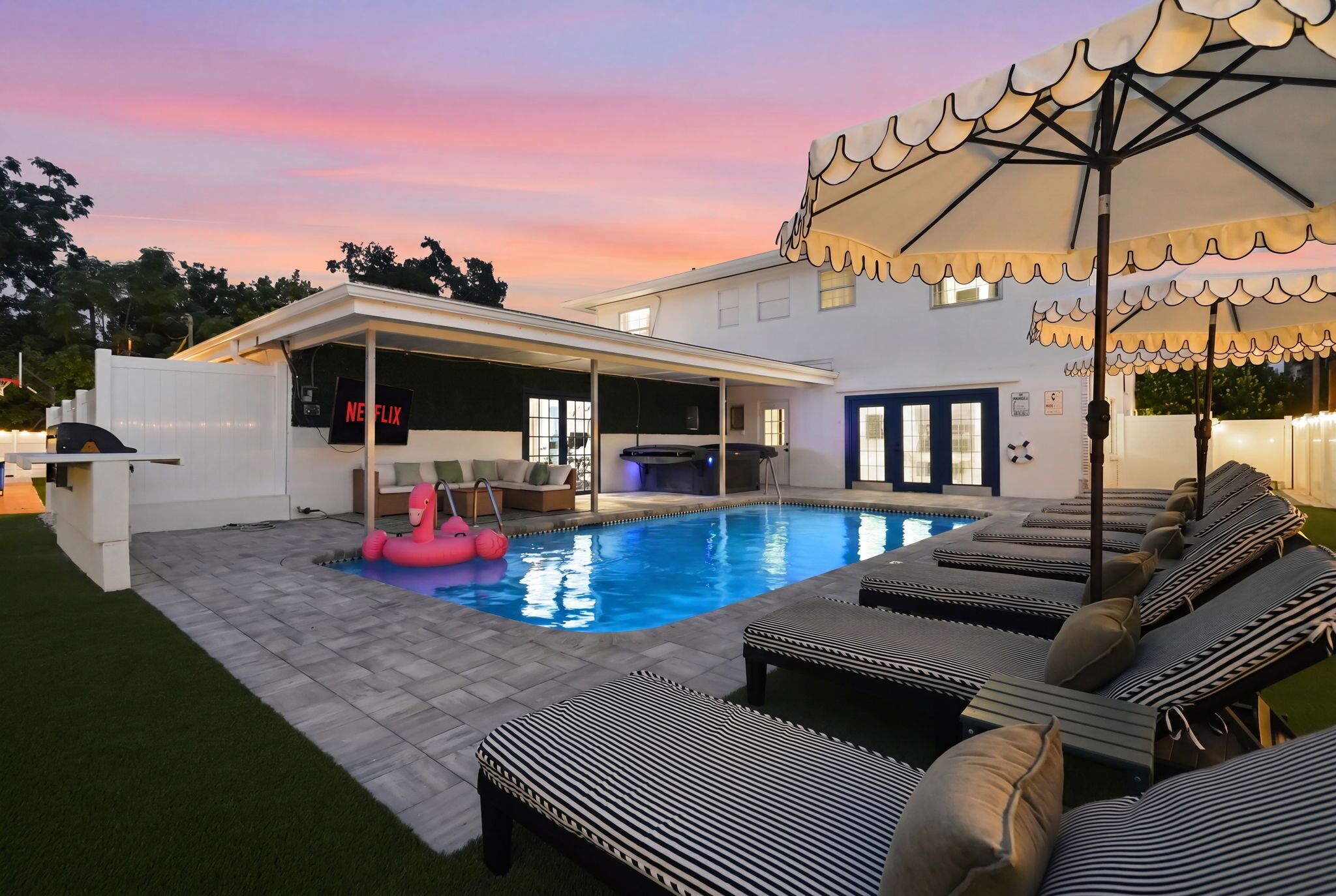 A swimming pool with lounge chairs and a hot tub, surrounded by a covered patio area.