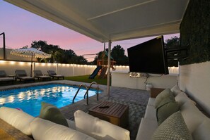 A covered outdoor area with a pool, lounge chairs, a children's play structure, and a flat-screen TV. - Sauna, Pickleball, Heated Pool, gym, Hot Tub and Games Retreat! (Largo)