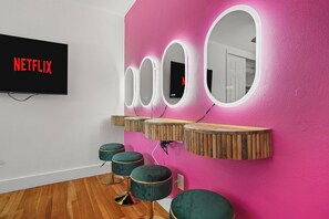 A room with a pink wall, a mounted TV displaying 'NETFLIX', and three mirrors with wooden shelves. - Sauna, Pickleball, Heated Pool, gym, Hot Tub and Games Retreat! (Largo)