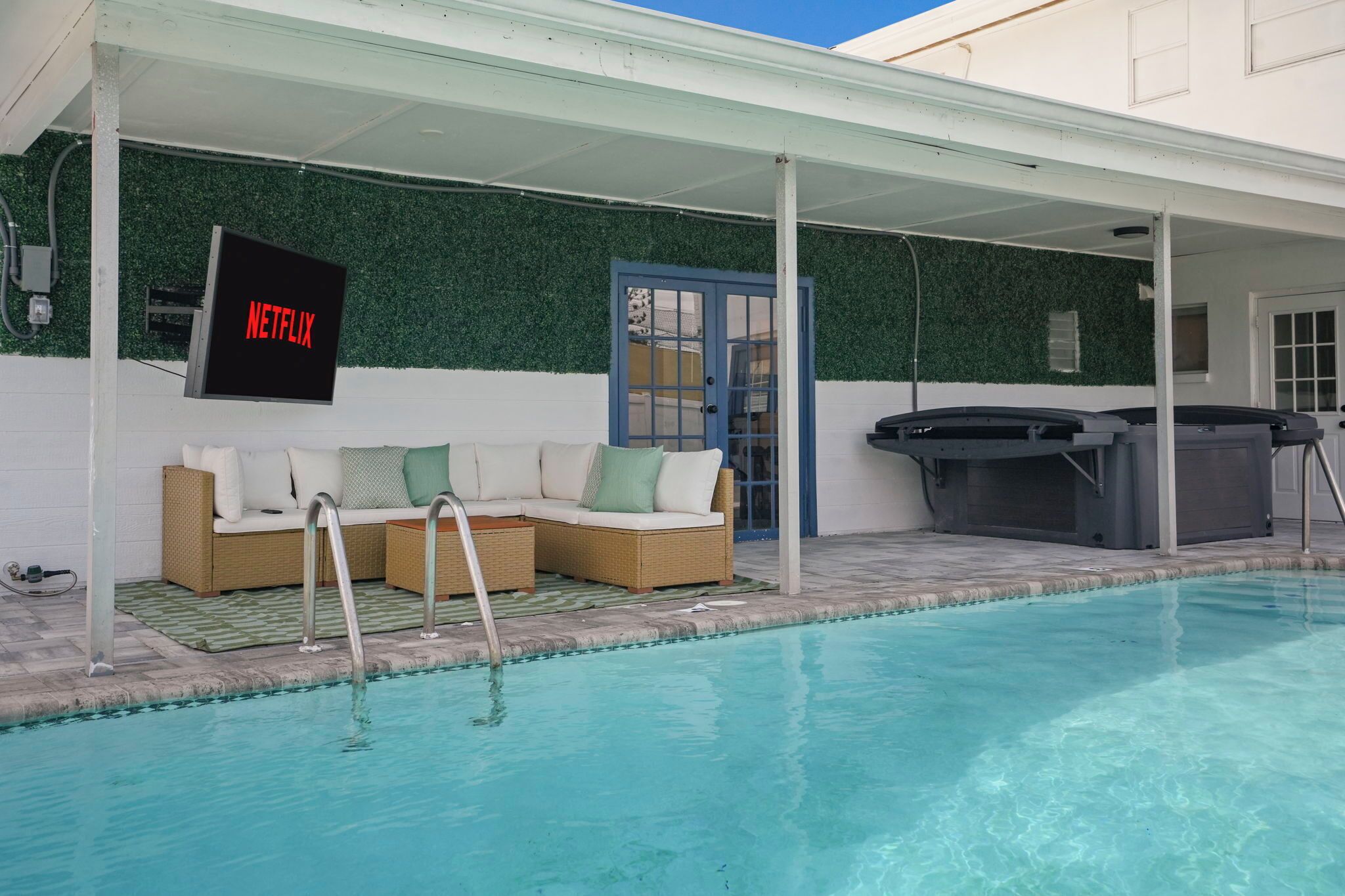 A pool area with a sofa and a Netflix sign, a covered seating area, and a hot tub.