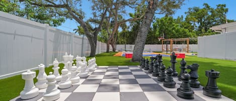 A chessboard set up on a grassy lawn with trees in the background.