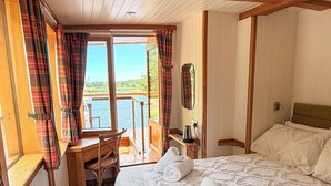 A bedroom with a bed, a desk, and a view of a body of water.