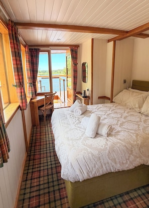 A bedroom with a bed, a desk, and a view of a body of water.