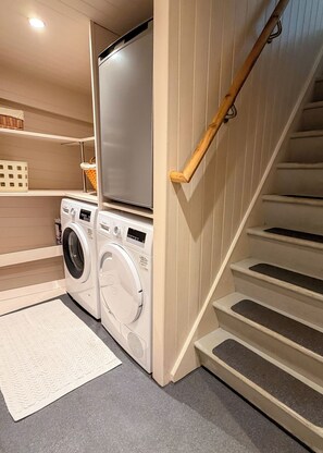 A laundry area with a washing machine and dryer, a wooden staircase, and a shelf with baskets.