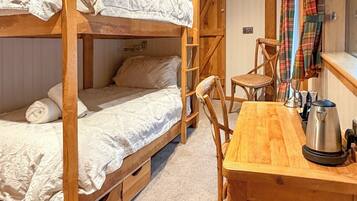 Habitación con literas, un escritorio de madera y una silla, una tetera y una cortina a cuadros.