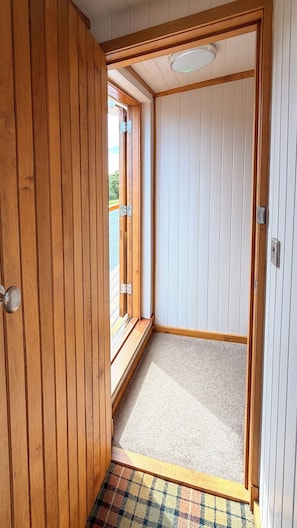 A wooden door leading to a room with a carpeted floor and a view of the outdoors.